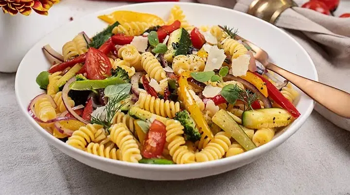 Frühlings-Nudelpfanne mit Spiralenpasta und Gemüse auf einem Teller vor der Packung Spiralenpasta auf gedecktem Tisch