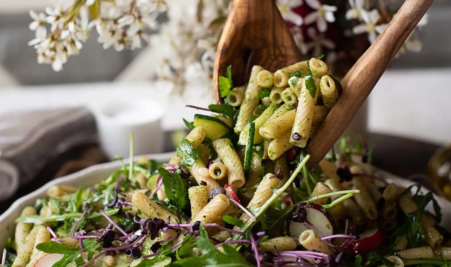 Frühlings-Nudelsalat mit Radieschen, frischen Kräutern und Gemüse, mit Holzbesteck serviert