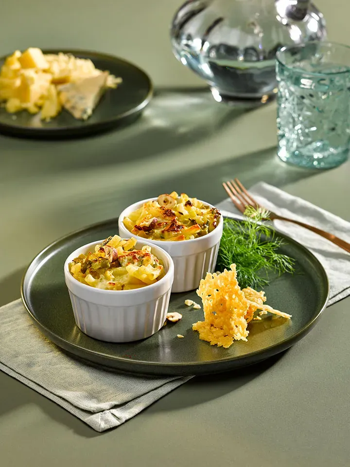 Cremige Mac and Käse, gratiniert in zwei Auflaufförmchen mit Käsechips auf einem Teller, Gastrorezept