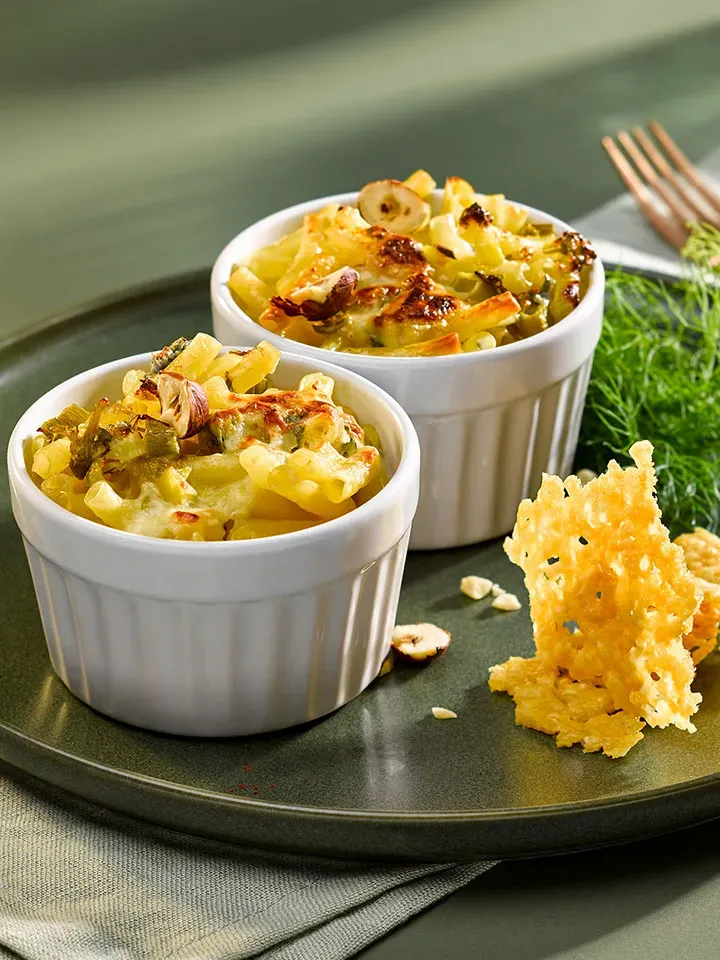 Cremige Mac and Käse in zwei Auflaufförmchen mit Käsechips auf einem Teller, Gastrorezept