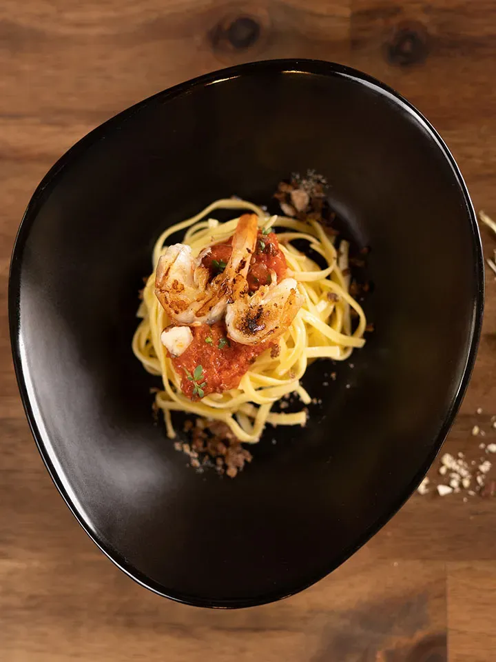 Fettuccine Pomodoro mit Alpengarnele und Feigenchutney auf schwarzem Teller auf Holztisch