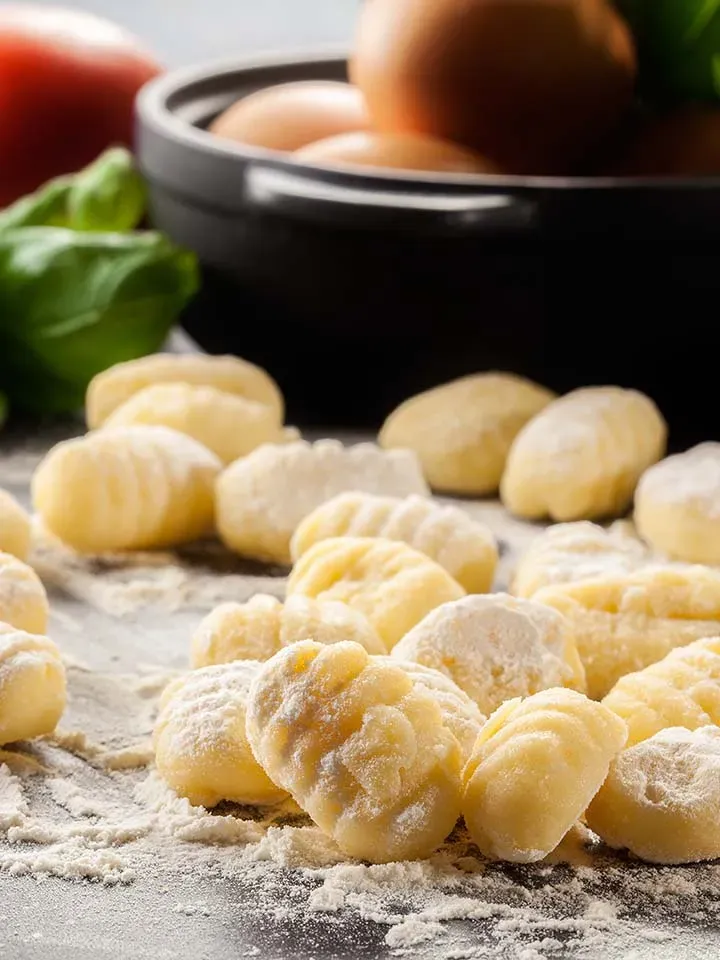 Hausgemachte Gnocchi aus Hartweizengrieß auf bemehlter Oberfläche, im Hintergrund Eier und Basilikum