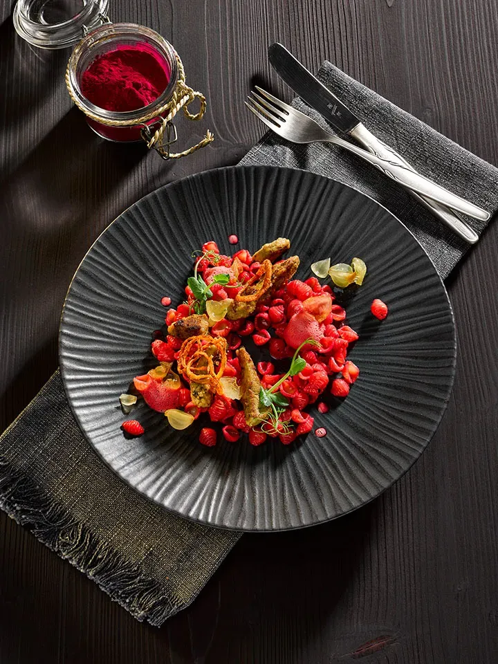 Kalbsleber mit Roter Beete und Muschelnudeln, kunstvoll auf schwarzem Teller mit Besteck und Gewürzglas