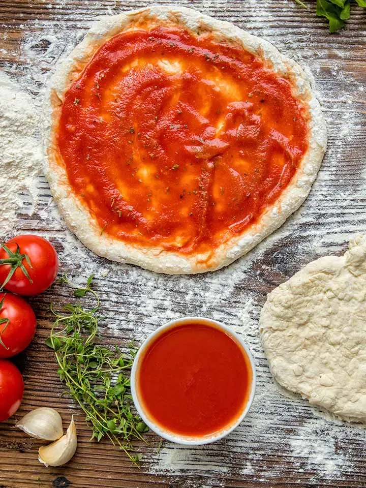 Krosser Pizzateig aus Hartweizengrieß, mit Tomatensauce bestrichen und frisch belegt, auf Holz