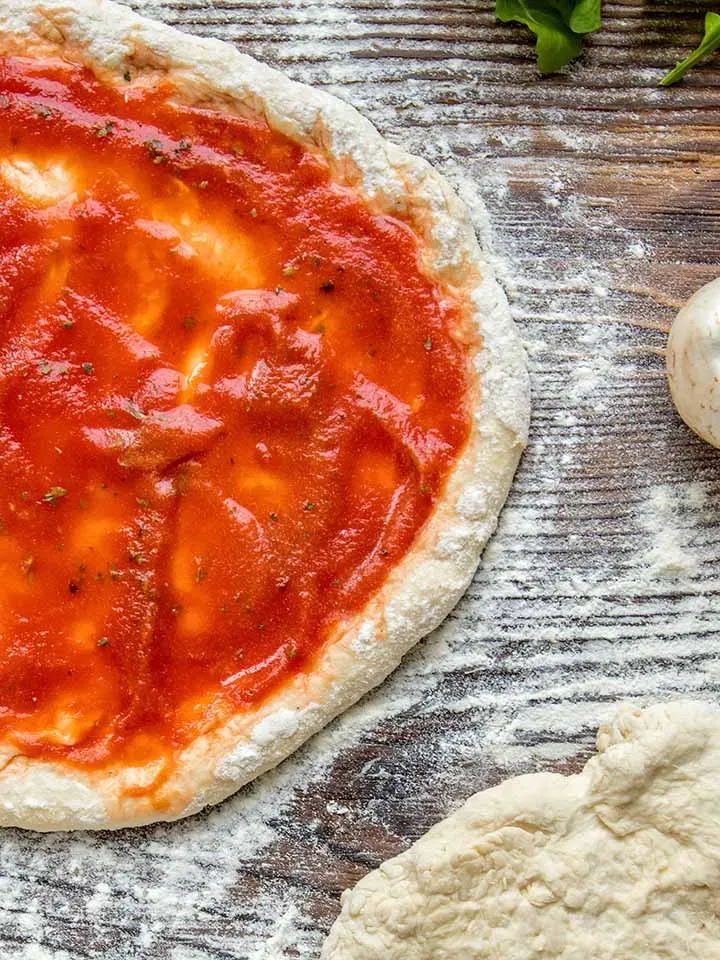 Krosser Pizzateig mit Tomatensauce auf bemehltem Holzuntergrund, Gastrorezept