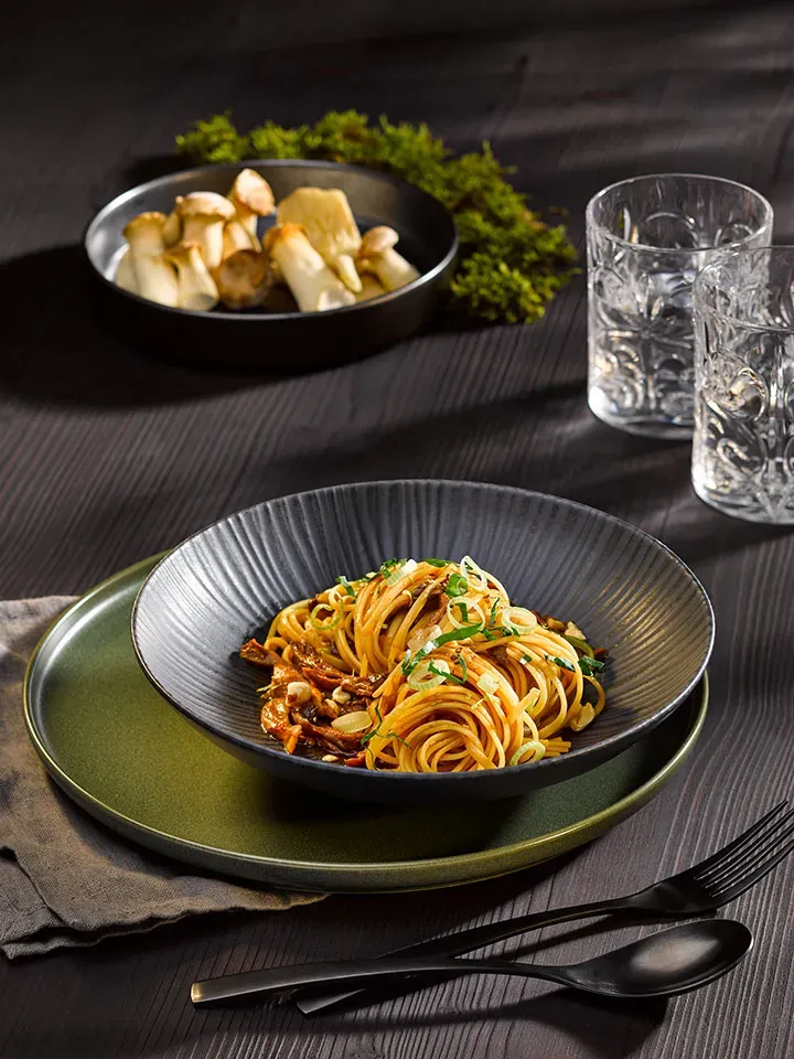 Pulled-Pilz-Linguine: Spaghetti mit Pilzen auf dunklem Tisch mit Besteck und Wassergläsern