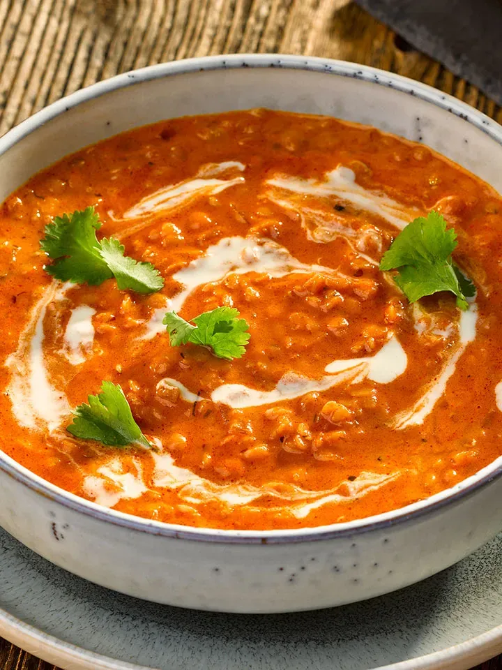 Rotes Linsen-Dal mit Kokosmilch: Schüssel mit cremigem Linsencurry, Sahne und Korianderblättern