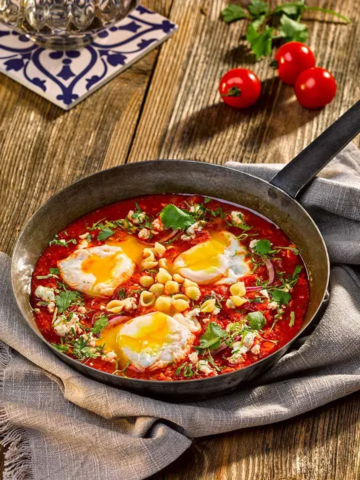 Shakshuka aus Tomatensauce, Eiern und Kichererbsen in der Pfanne auf Holzuntergrund