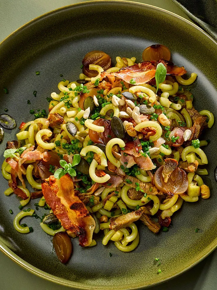 Steirischer Nudelsalat mit Äpfeln, Speck, Pilzen, Kräutern und Samen auf Teller