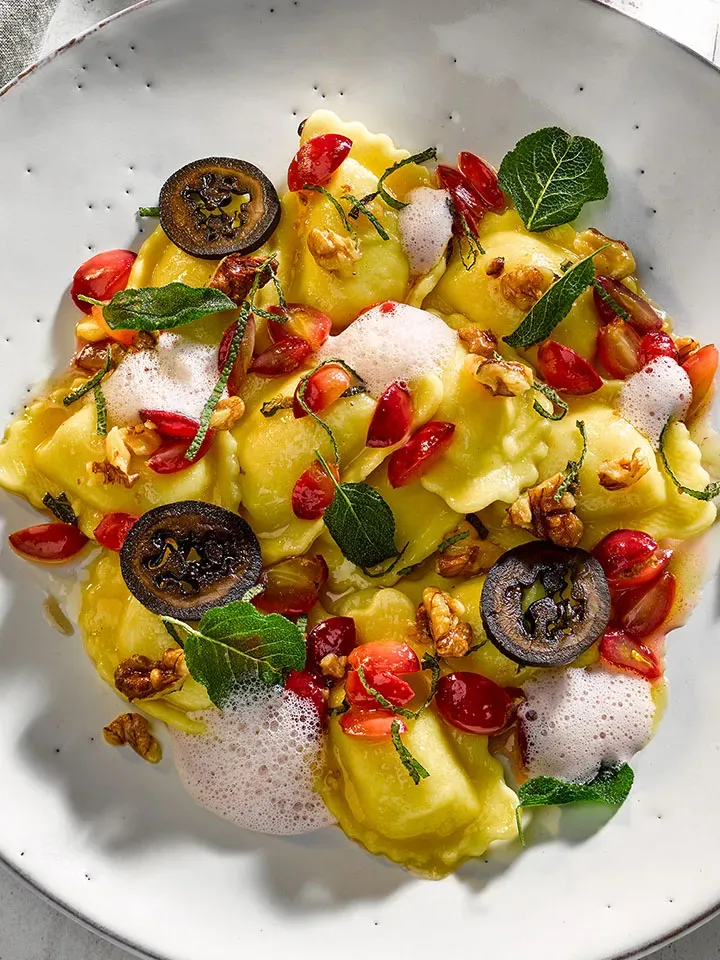 Tiroler Schlutzkrapfen mit Walnüssen, Tomaten, Salbeiblättern und Schaum auf Teller