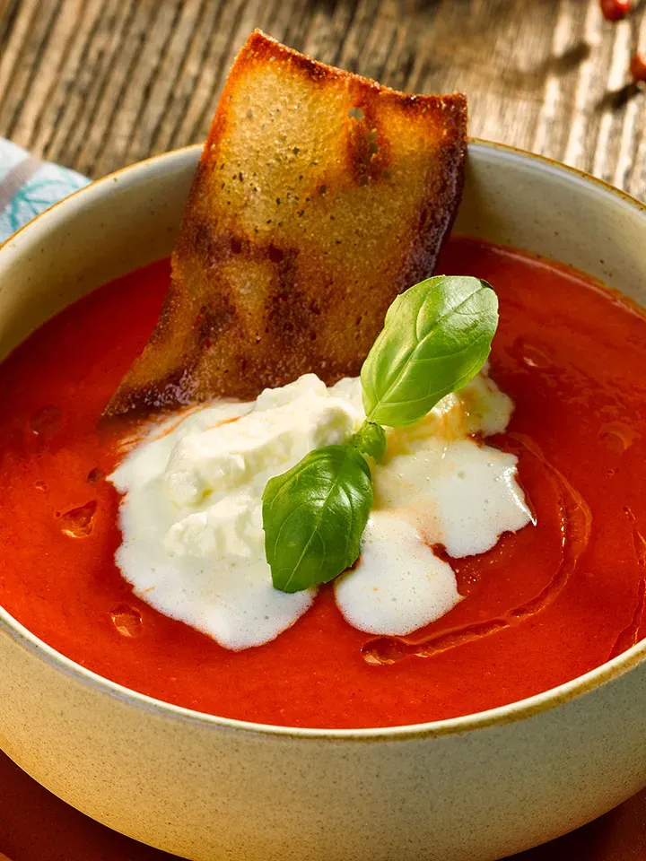 Tomatensuppe mit Gin-Sahne, Basilikum und geröstetem Brot in einer Schale