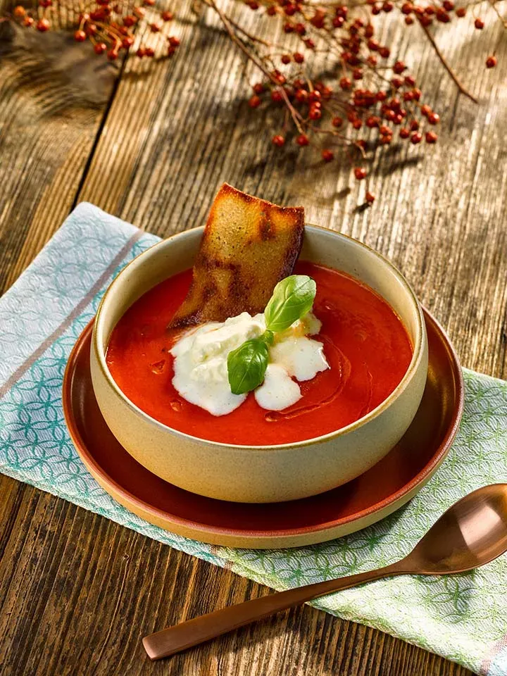 Tomatensuppe mit Gin-Sahne, Basilikum und geröstetem Brot in einer Schale auf Holztisch