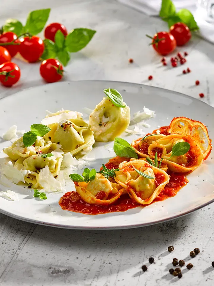 Tortelloni-Duett mit Sugo: Teller mit Tortelloni, teils in Tomatensauce, mit frischen Kräutern