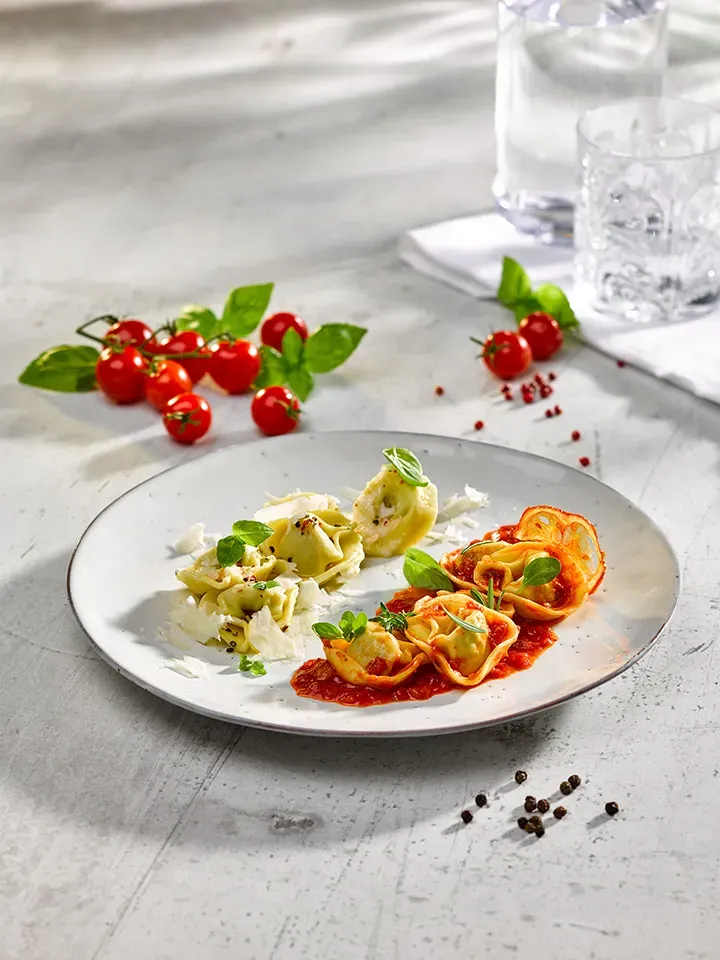 Tortelloni-Duett: Teller mit Tortelloni in Tomatensauce und Käse, daneben Kirschtomaten