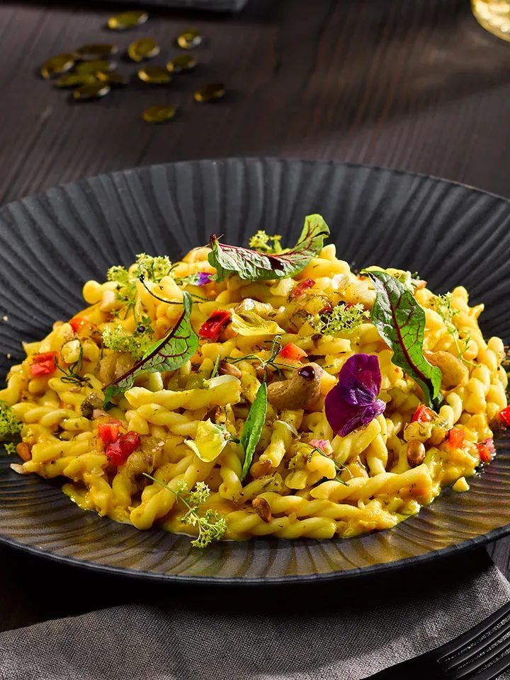 Treccine mit Kürbis-Sahne-Sauce, garniert mit Kräutern und essbaren Blüten