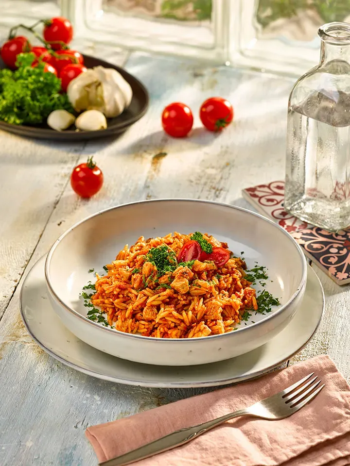 Nudelreisfleisch mit Tomaten auf einem hellen Holztisch mit Wasserflasche, Gastrorezept