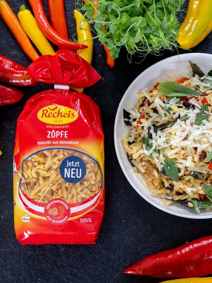 Gedrehte Nudeln mit Arrabbiata in einer Schüssel neben Packung Zöpfe und frischen Chilischoten