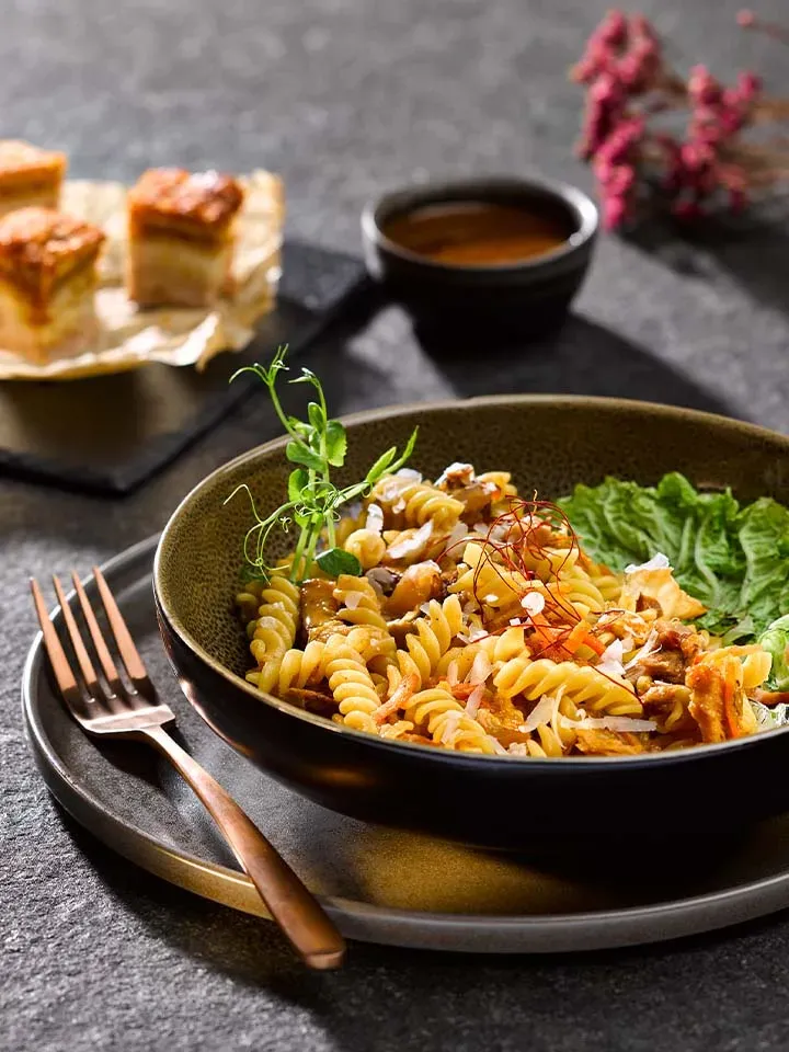 Gericht mit Kimchi: Fusilli, Salat und Kräuter auf einem Teller, daneben Gabel und kleine Küchlein