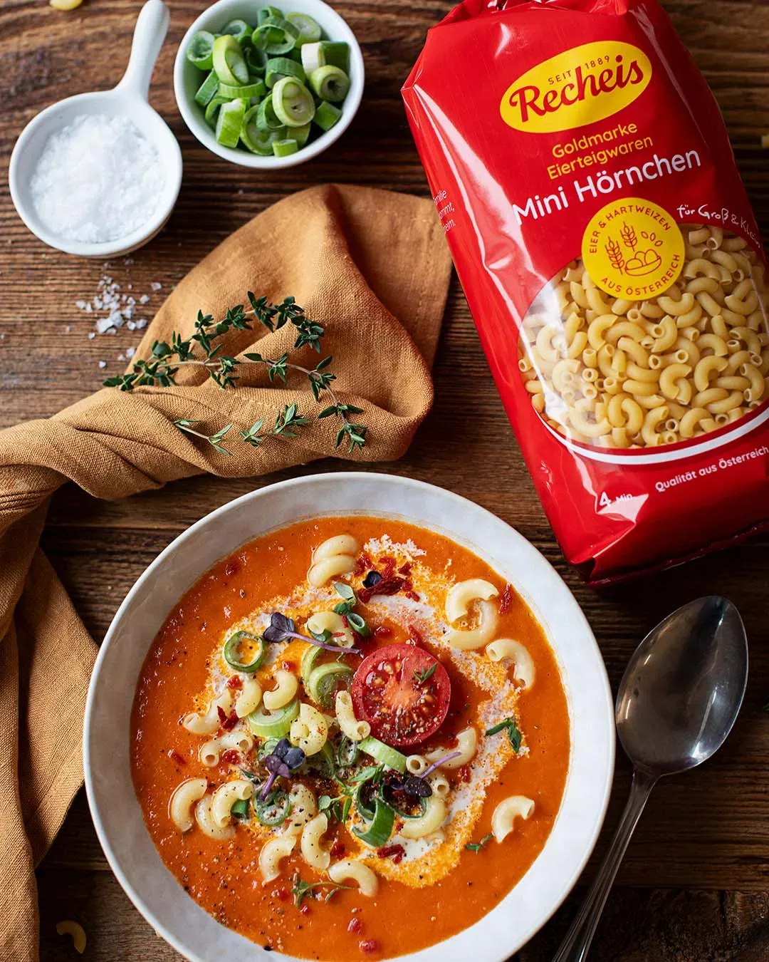 Geröstete Tomatensuppe mit Mini-Hörnchen und frischen Kräutern auf einem Teller auf Holztisch