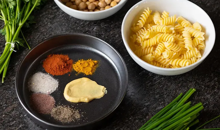Gewürze, Kichererbsen und Nudeln für veganen Eiersalat auf dunklem Untergrund