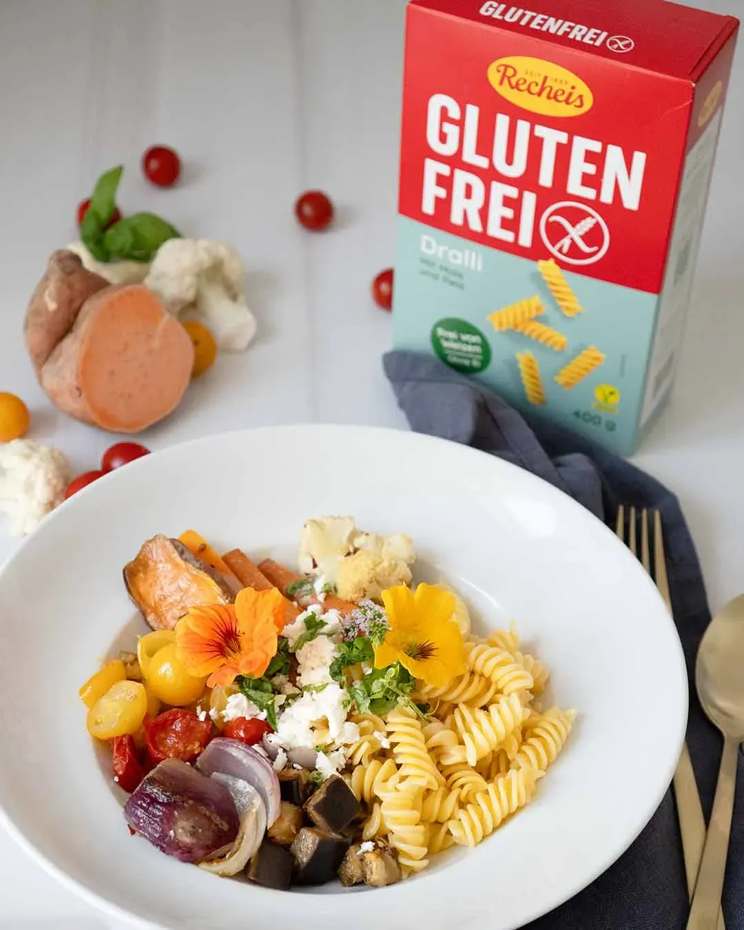 Glutenfreie Dralli-Nudelbowl mit Gemüse und essbaren Blüten neben einer Packung glutenfreier Nudeln