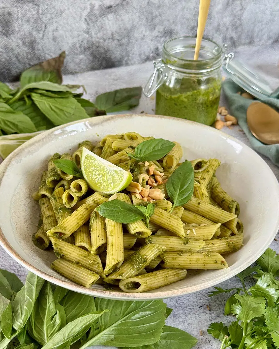 Glutenfreie Penne mit Thai-Basilikum-Pesto auf einem Teller, garniert mit Limettenscheibe und Kräutern