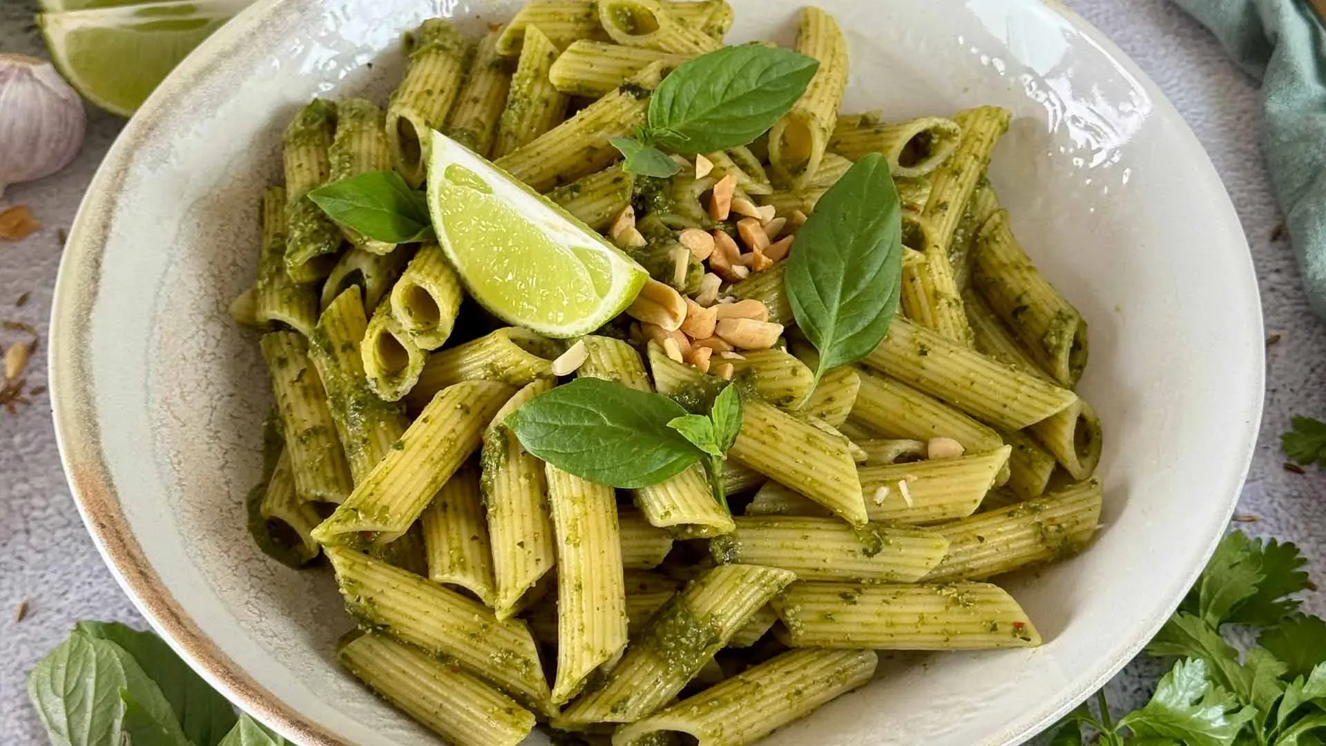 Glutenfreie Penne mit Thai-Basilikum-Pesto, garniert mit Limettenscheibe und Basilikumblättern, im Querformat