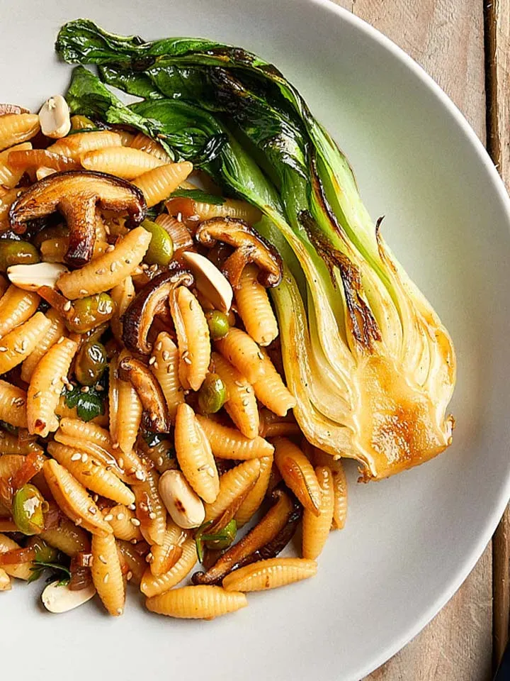 Gnocchi sardi als Asia-Nudelpfanne mit gebratenem Pak Choi, Pilzen und Erbsen auf einem Teller