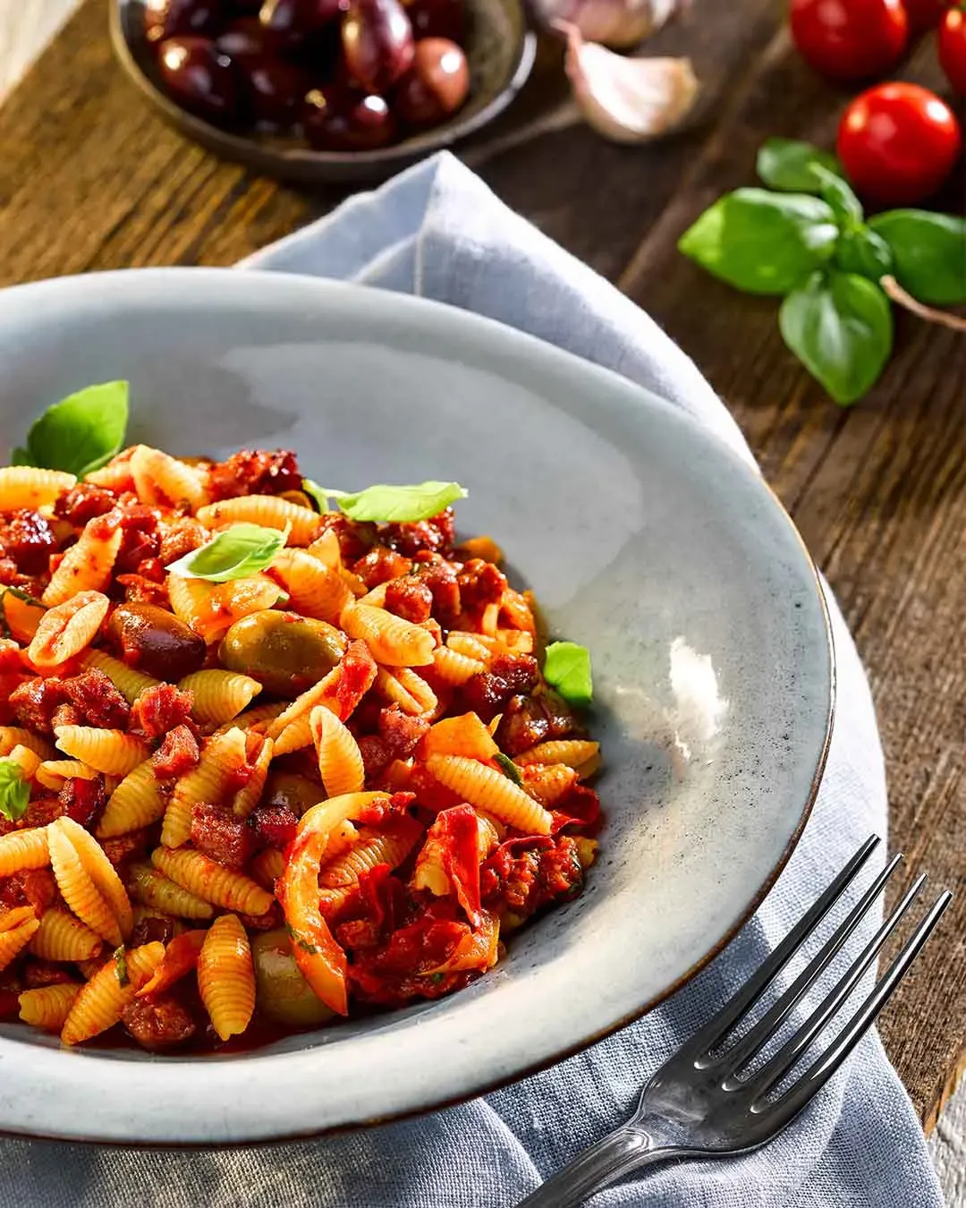 Gnocchi sardi mit Salsiccia in Tomatensauce mit Oliven und Basilikum auf einem Holztisch