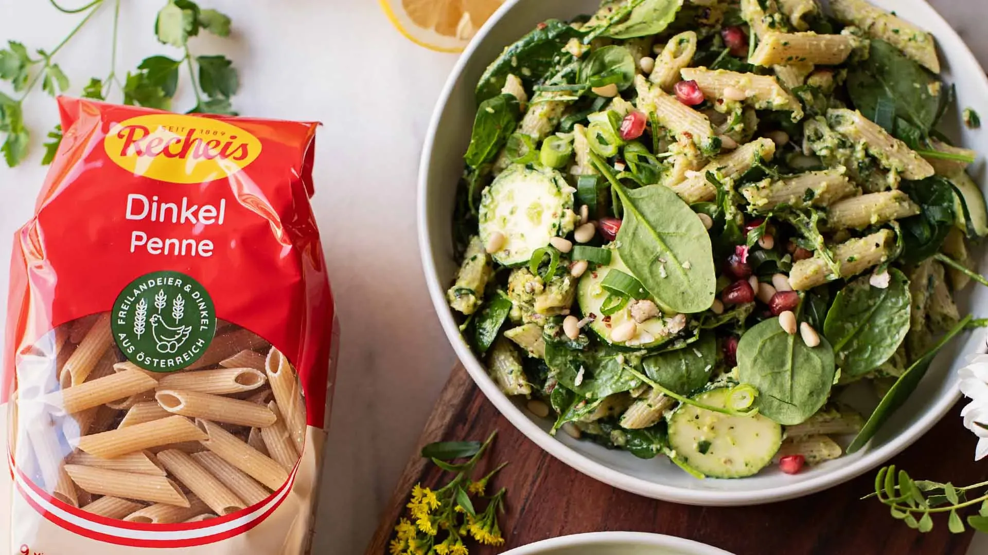 Green-Goddess-Superfood-Nudelsalat mit Dinkelpenne, Spinat, Gurken und Granatapfel in einer Schale neben der Dinkel-Penne-Packung