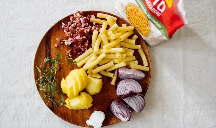 Zutaten für Grenadiermarsch auf einem Holzbrett: Nudeln, Zwiebeln, Kartoffeln, Speck und Kräuter