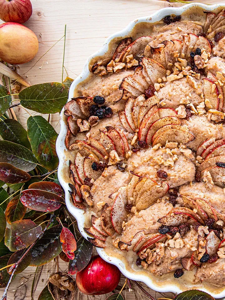 Grießnockerl-Auflauf mit Äpfeln, Nüssen und Rosinen in einer weißen Backform auf Holztisch