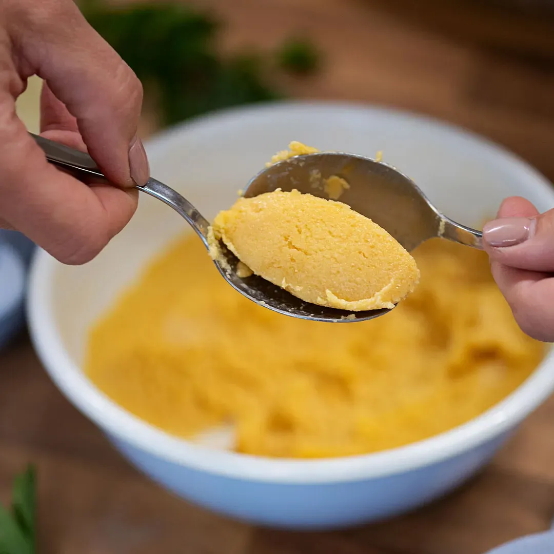 Grießnockerl formen: zwei Hände formen mit Löffeln eine Portion gelben Teig
