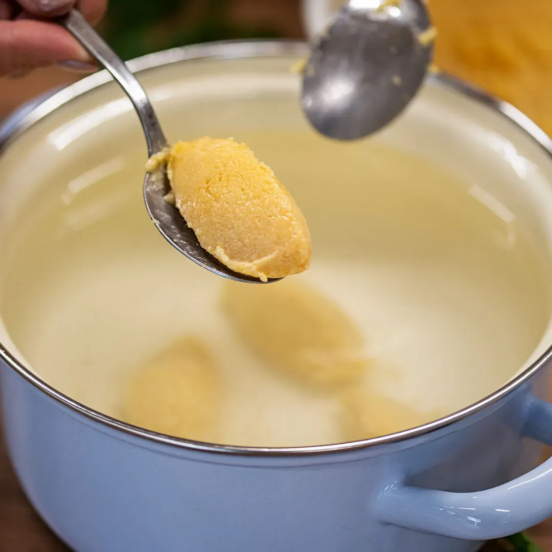 Grießnockerl kochen: Löffel mit Teig wird über einen Topf mit Wasser gehalten