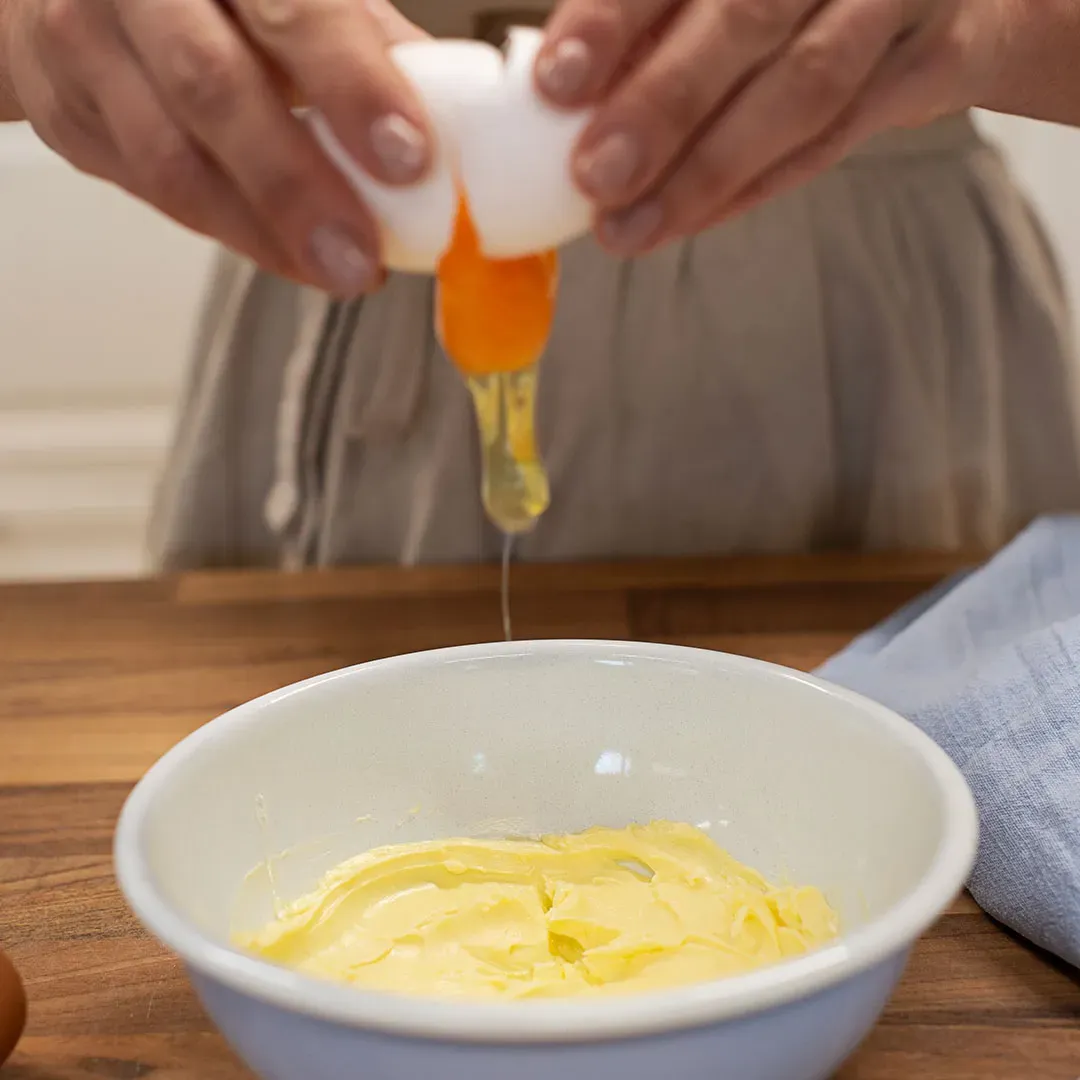 Grießnockerl mit Ei: Person schlägt ein Ei über einer Schüssel mit Butter auf
