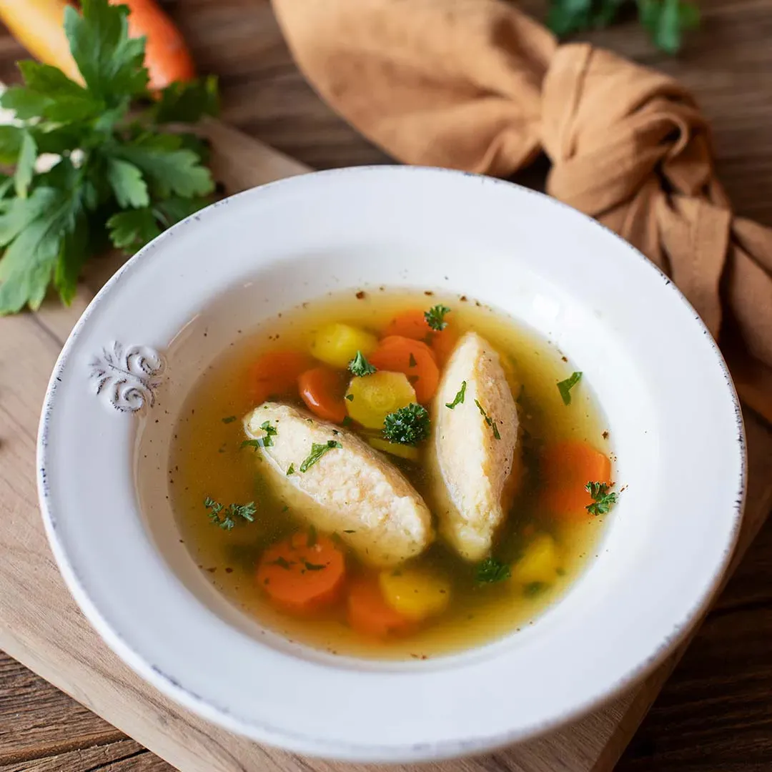Grießnockerlsuppe mit Karotten, Gemüse und zwei Nockerl, mit Kräutern garniert, auf einem Teller