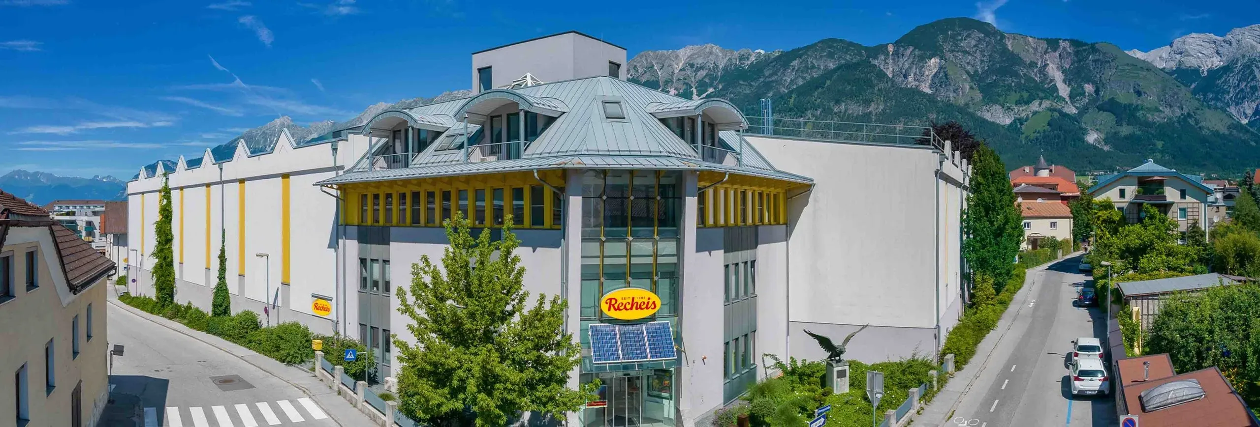 Recheis Haupthaus mit Logo vor Bergkulisse und klarem Himmel