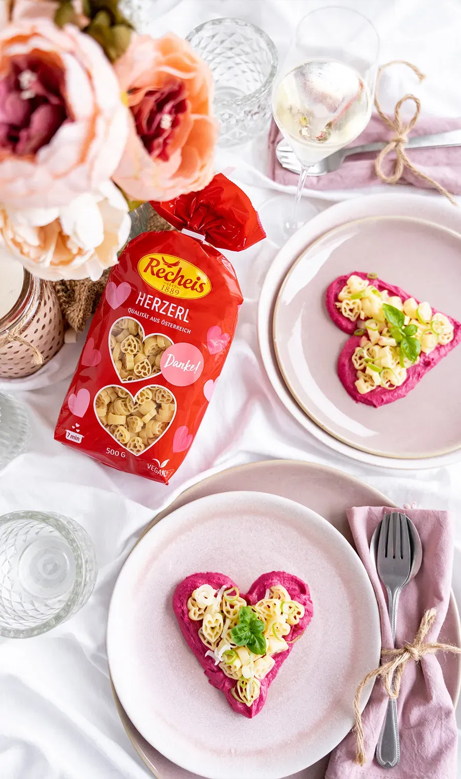 Valentinstagsrezept: Herzerl auf Rote-Bete-Hummus mit Harissadressing auf rosa Tellern, daneben rote Packung und Blumen
