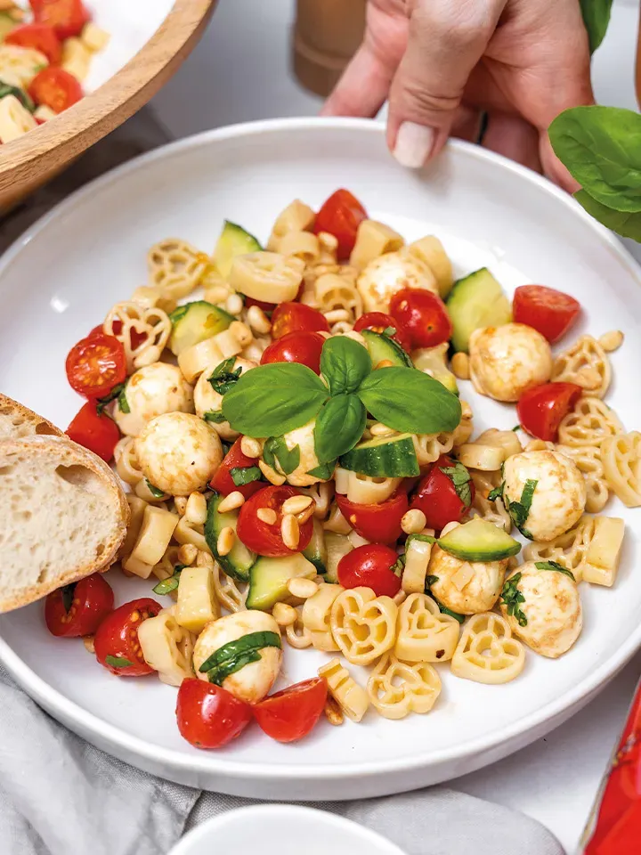 Herzerl-Caprese-Nudelsalat mit Tomaten, Mozzarella, Gurken und Basilikum auf einem Teller