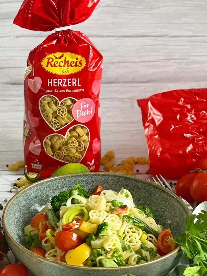 Herzerl-Nudel-Frühlingspfanne in einer Schüssel neben roter Packung Recheis Herzerl Nudeln
