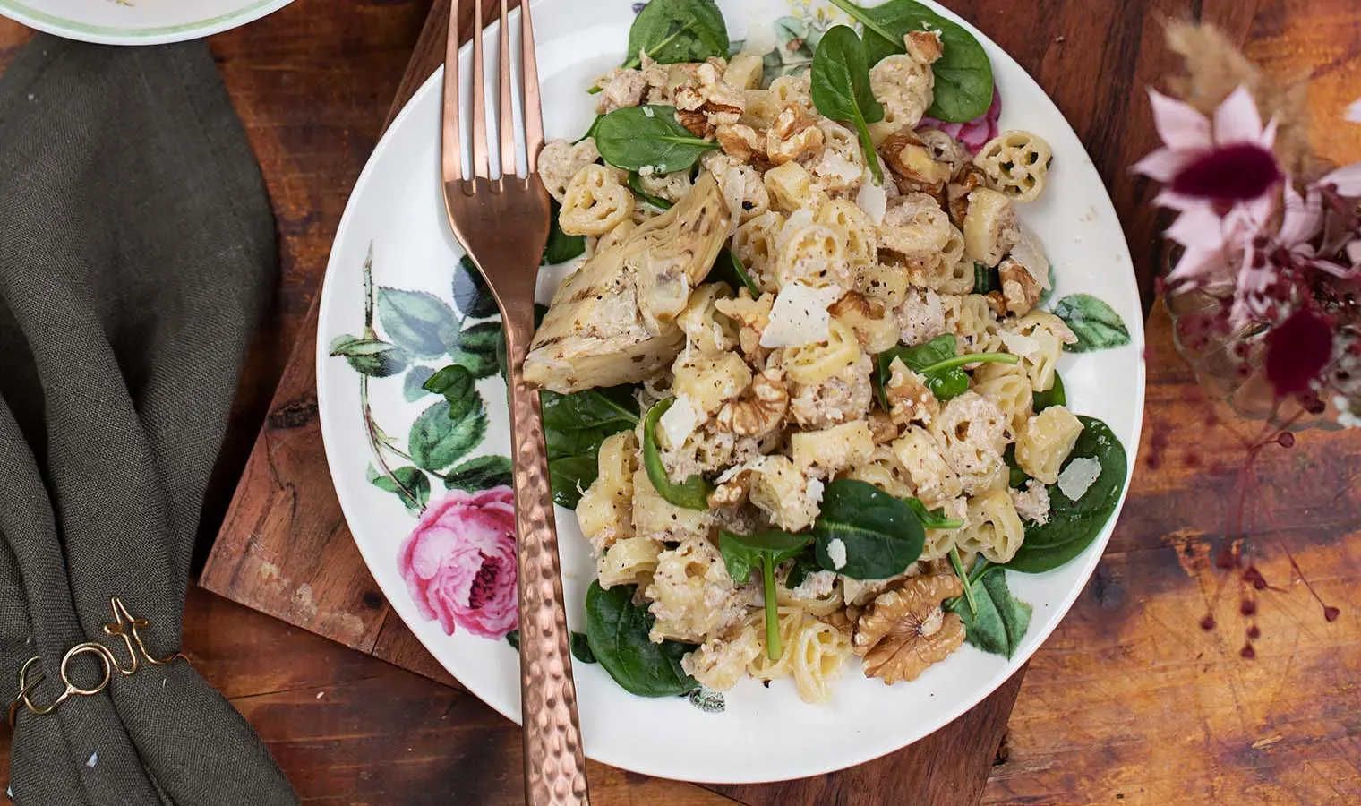 Herzerl-Nudeln mit Artischocken-Pesto, Spinat und Walnüssen auf einem Teller auf Holztisch