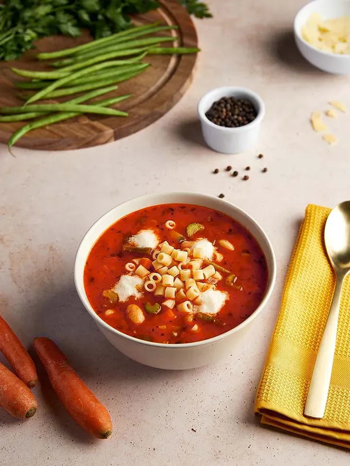 Herzhafte Minestrone mit Ditalini in einer Schüssel, daneben Karotten und Gewürze