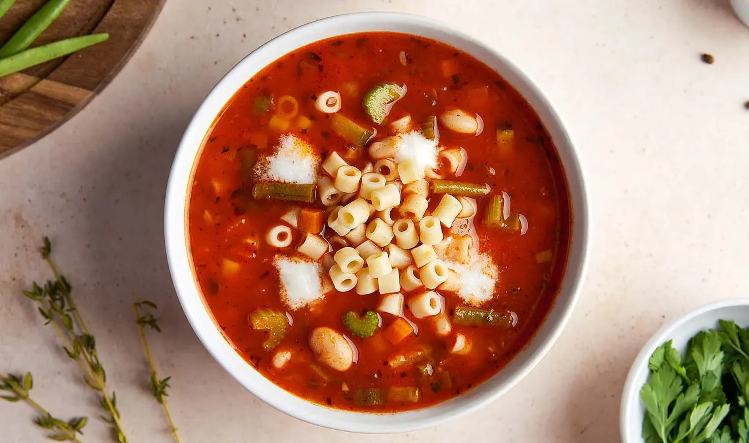 Herzhafte Minestrone mit Ditalini und Gemüse in einer Schüssel auf hellem Untergrund, Frontalansicht