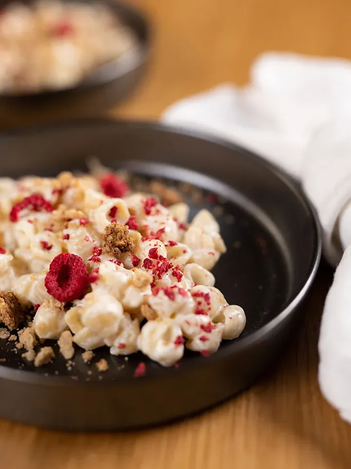 Honig-Milchnudeln mit getrockneten Himbeeren als Süßspeise auf schwarzem Teller auf Holztisch