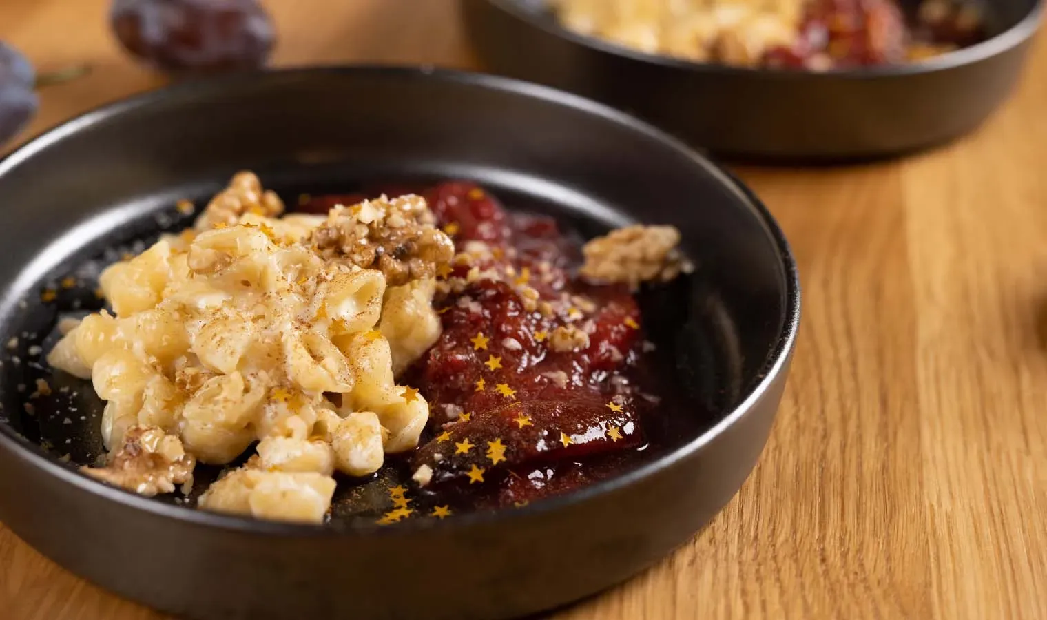Honig-Milchnudeln mit Zwetschgenröster als Weihnachtsrezept: Nudeln mit Walnüssen und roter Soße in schwarzer Schale