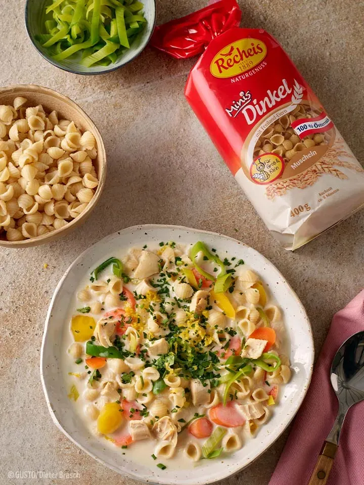 Hühnersuppentopf mit Muschelnudeln in cremiger Gemüsesuppe auf Teller, daneben Schale und Packung