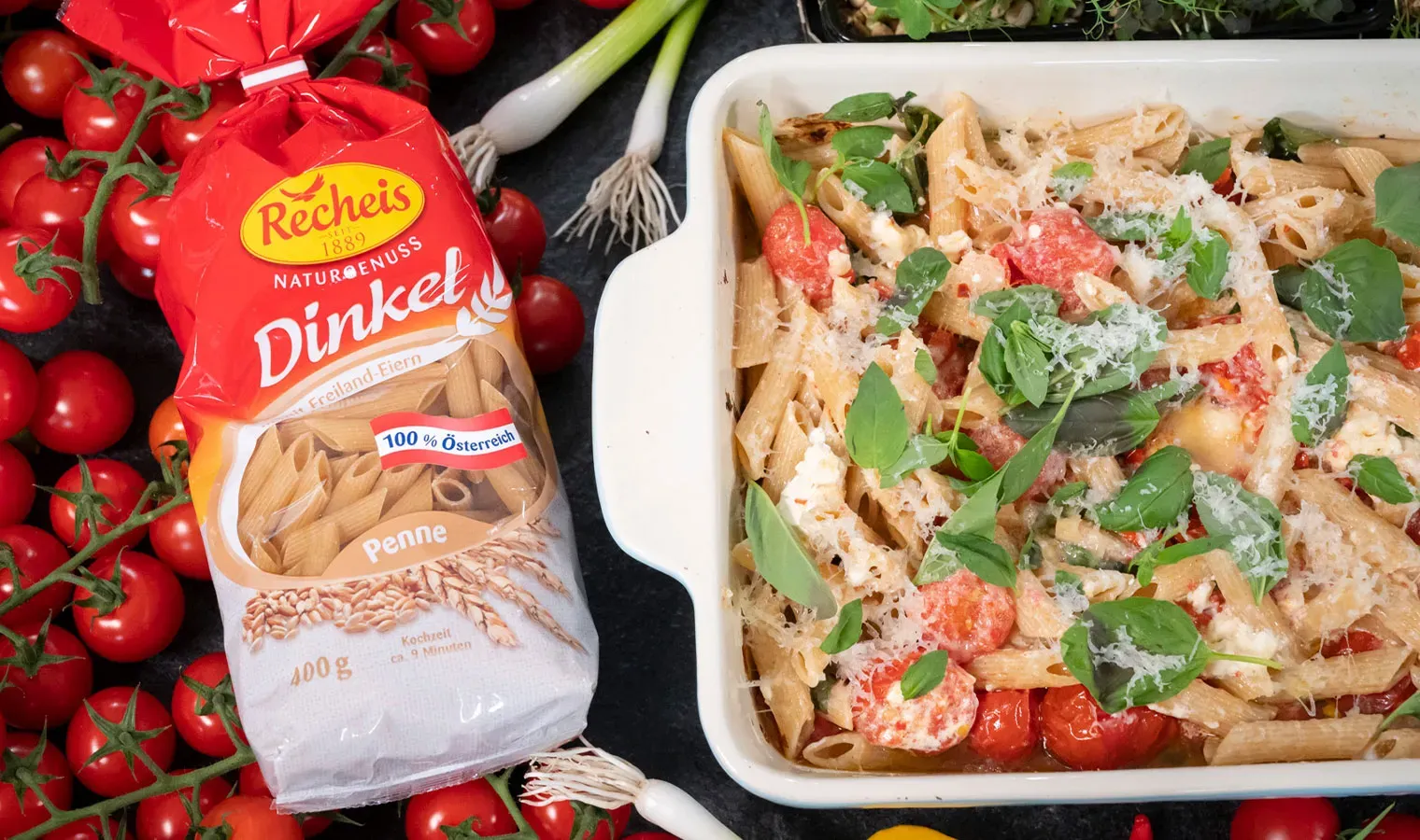 Im Ofen geschmorte Paradeiser mit Feta und Penne in Auflaufform neben Packung Recheis Dinkel-Penne