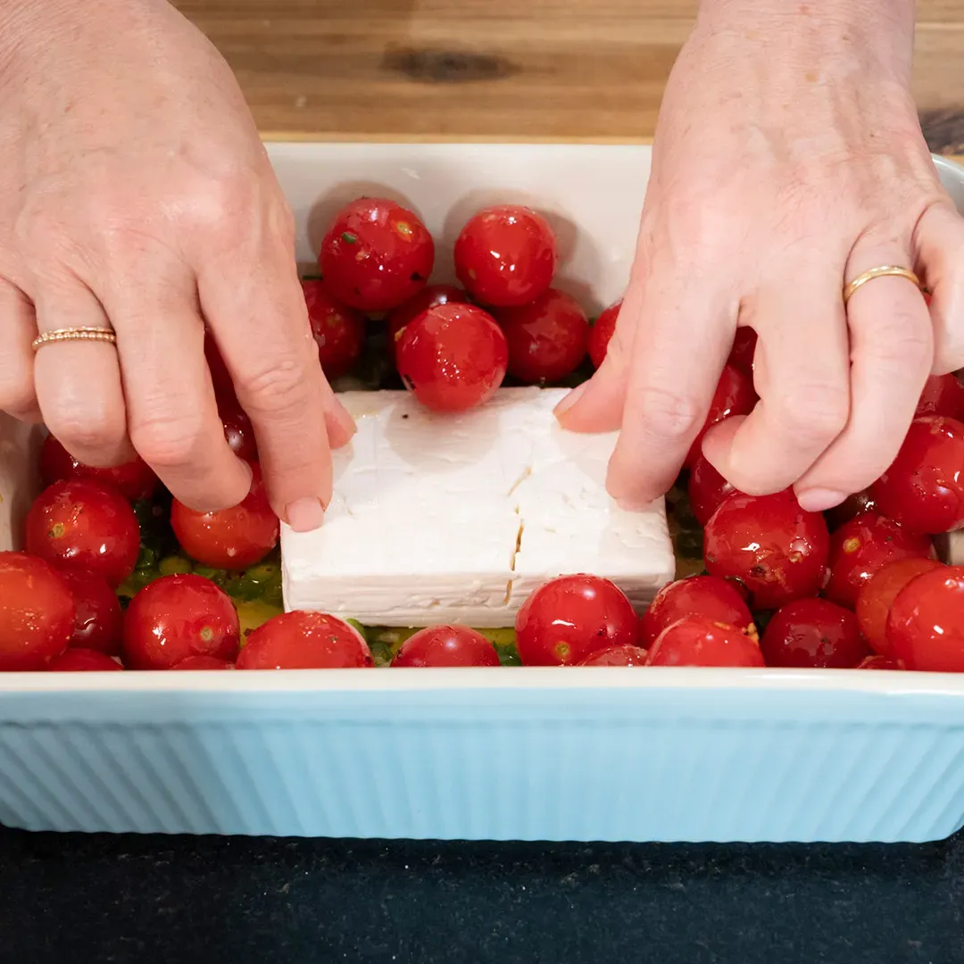 Hände legen Kirschtomaten um einen Block Feta in einer Auflaufform