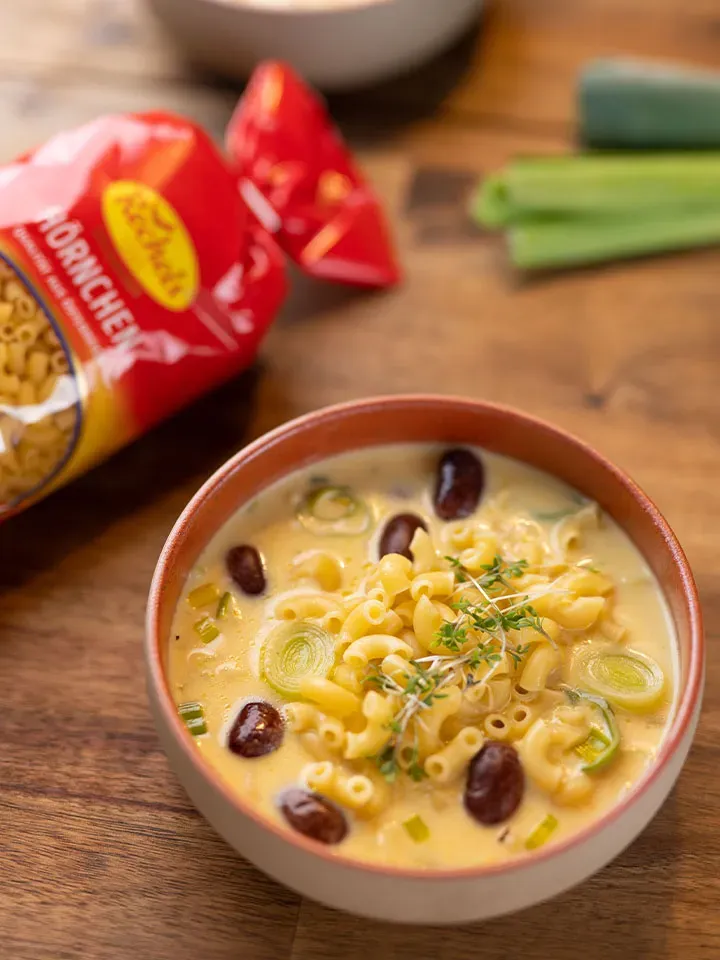 Einfache Käse-Lauch-Suppe mit Nudeln, Bohnen und Kräutern in einer Schüssel auf Holztisch