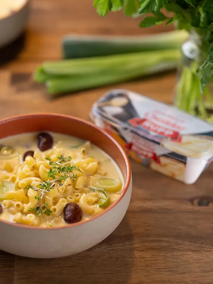 Käse-Lauch-Suppe mit Nudeln und frischen Kräutern in einer Schüssel auf Holztisch